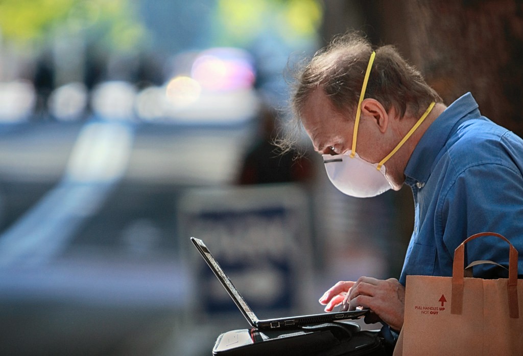 Man met een gezichtsmasker werkt op laptop