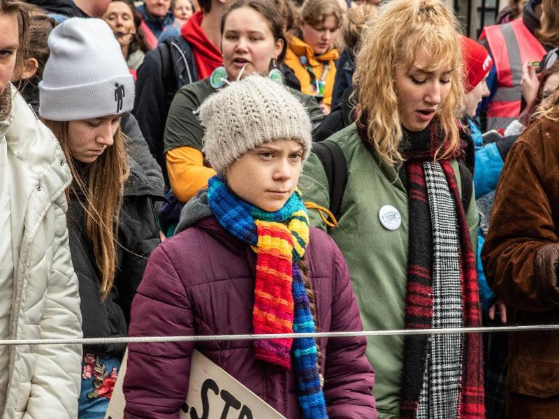 Greta Thunberg (met kleurrijke sjaal) in een protest